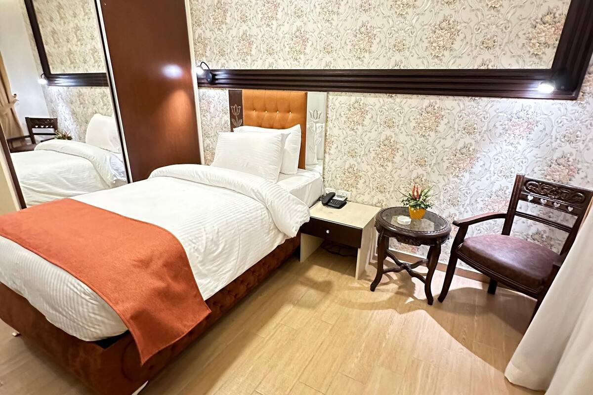 A hotel room with a bed, a desk, a chair, and a small table with a plant.