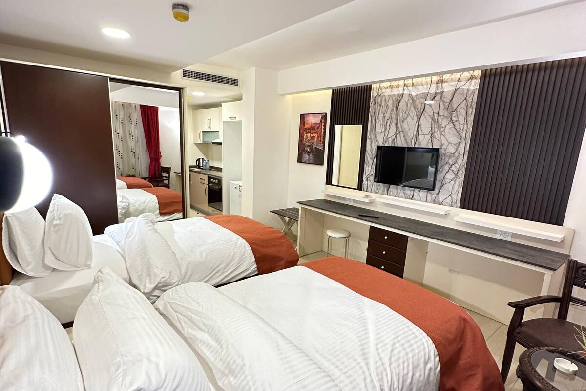 A hotel room with two beds, a desk, a mirror, and a TV.