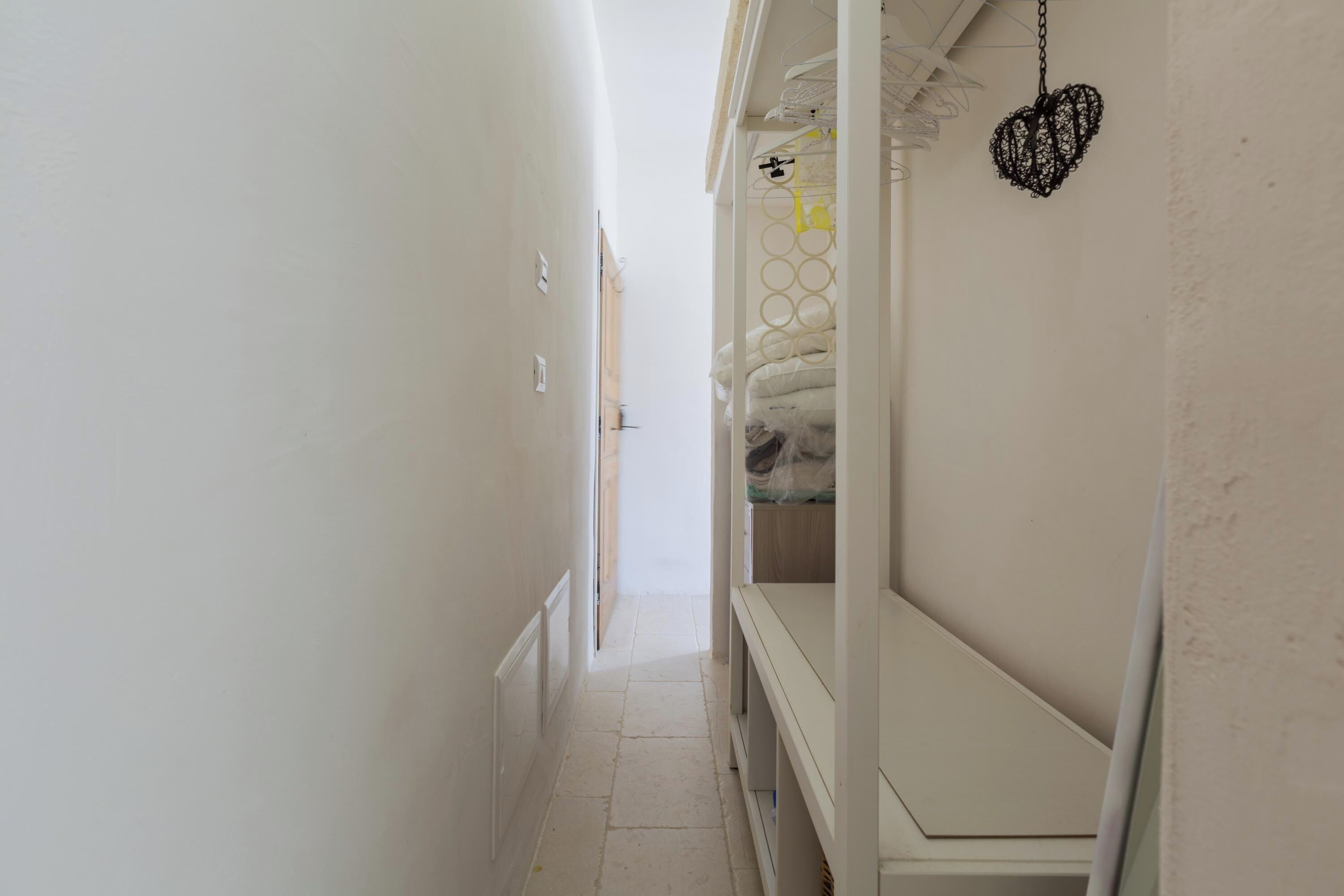 Ein schmaler Flur mit weißer Wand, einer Tür am Ende und einem Bett mit herzförmiger Dekoration an der Wand.