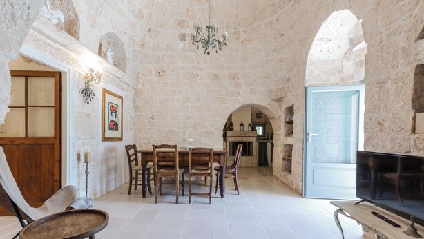 Une pièce aux murs de pierre, comprenant une table à manger, des chaises, un téléviseur et un lustre.