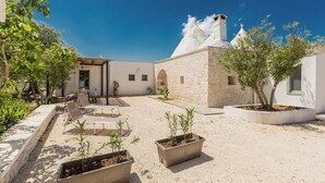 Une cour bordée de bâtiments en pierre, avec des espaces de repos en plein air et des plantes en pot.