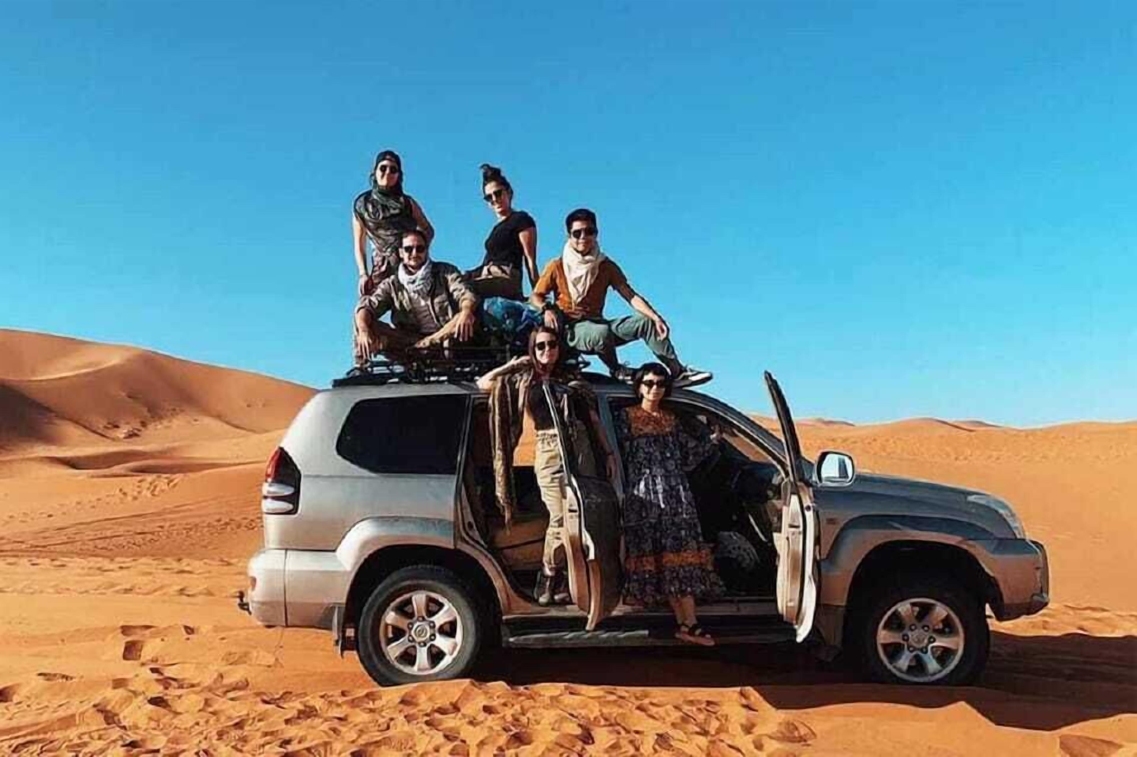 Un grupo de personas posando en un vehículo en un desierto, con dunas de arena al fondo.