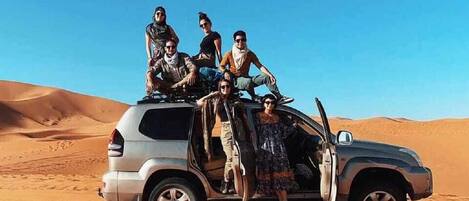 Un grupo de personas posando en un vehículo en un desierto, con dunas de arena al fondo.