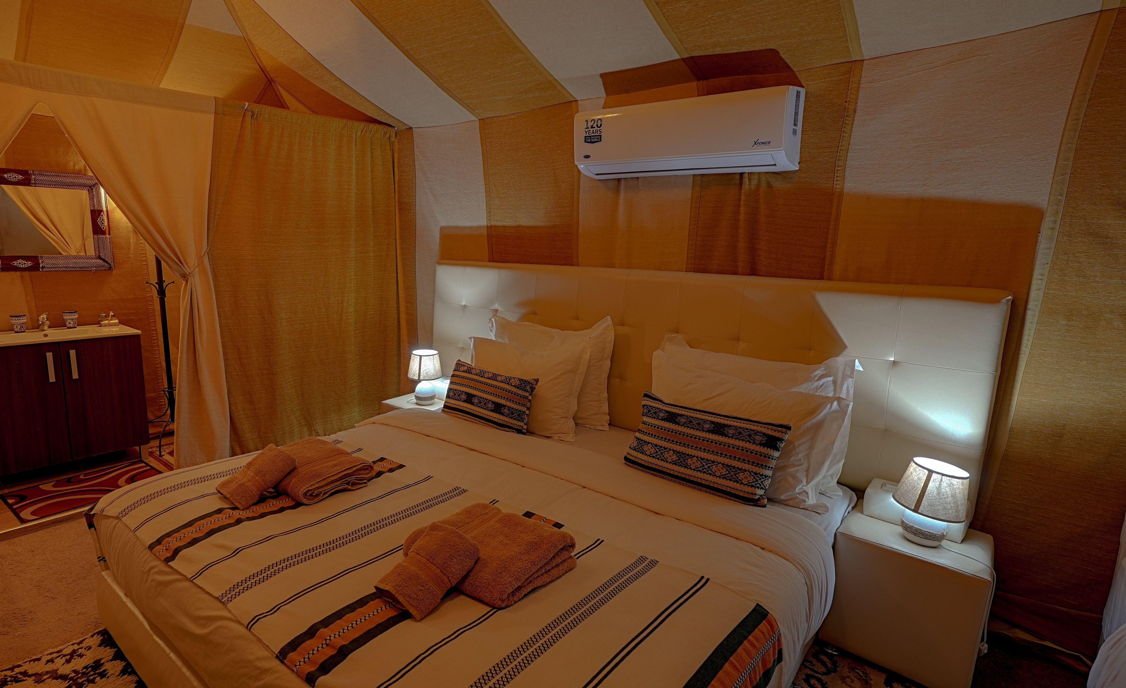 A hotel room with a bed, a nightstand, a mirror, a wardrobe, and an air conditioning unit.