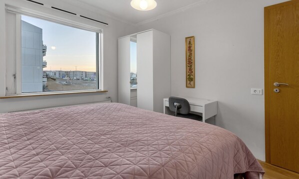 Une chambre avec un grand lit, un bureau, une chaise, une armoire et une fenêtre donnant sur la ville.