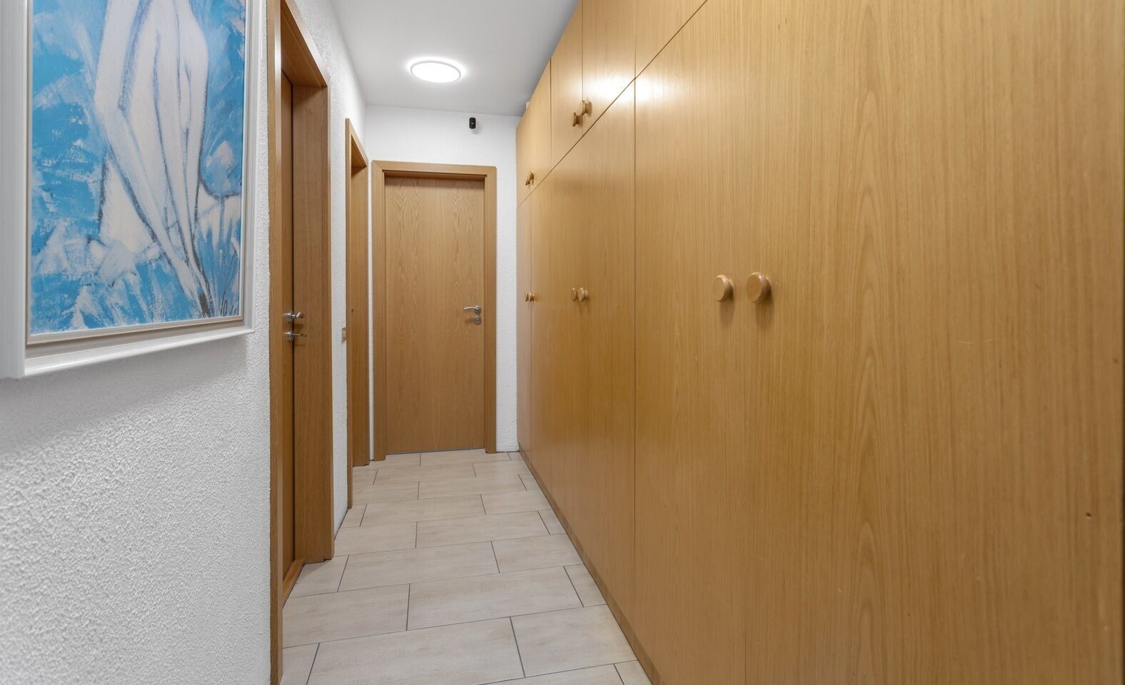 A hallway with wooden doors, a tiled floor, and a ceiling light.