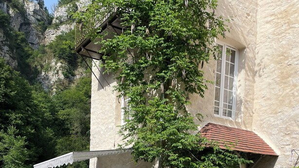 Ein Steinhaus mit überdachter Terrasse, Sitzgelegenheiten im Freien und Blumentöpfen.