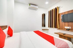A hotel room with a bed, a desk, a television mounted on the wall, and a window with curtains. - Hotel Apple Grand (Indore)