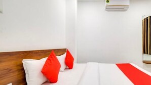 A modern hotel room with a wooden headboard, white bedding, and red accents.