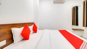 A hotel room with a wooden headboard, white bedding, and a red accent pillow. - Hotel Apple  (Indore)