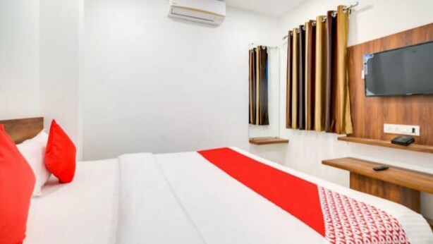 A hotel room with a bed, a desk, a television, and a window with curtains. - Hotel Apple  (Indore)