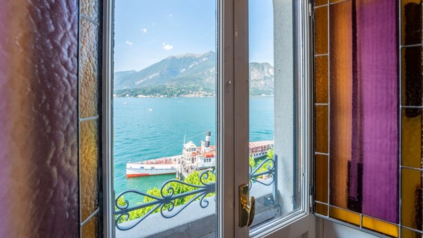 Ein Fenster mit Blick auf ein Gewässer, ein Boot und eine gebirgige Landschaft.