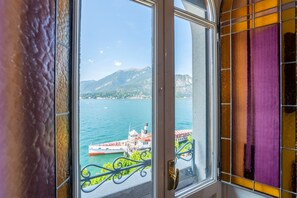 A window with a view of a body of water, a boat, and a mountainous landscape.