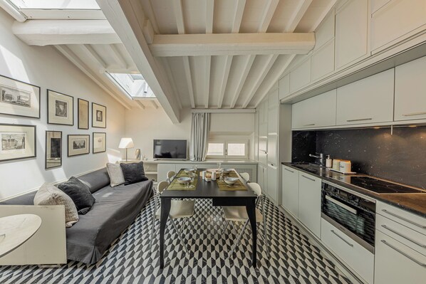 A compact living space with a dining area, kitchenette, and a sofa with cushions. - Rebecca Suite Florence (Firenze)