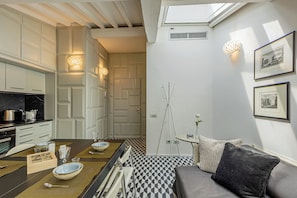 A compact kitchen with modern appliances, a dining area with a table set for two, and a cozy seating area with cushions.