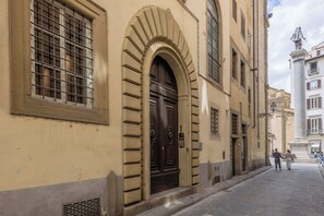 A building with a large arched entrance, a barred window, and a statue on a pedestal.