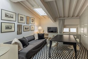 A modern room with a sofa, a dining table, chairs, a TV, and framed pictures on the wall. - Rebecca Suite Florence (Firenze)