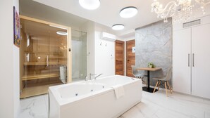 Un bagno moderno con una grande vasca, uno sporto doccia in vetro e un piccolo tavolo con una sedia.