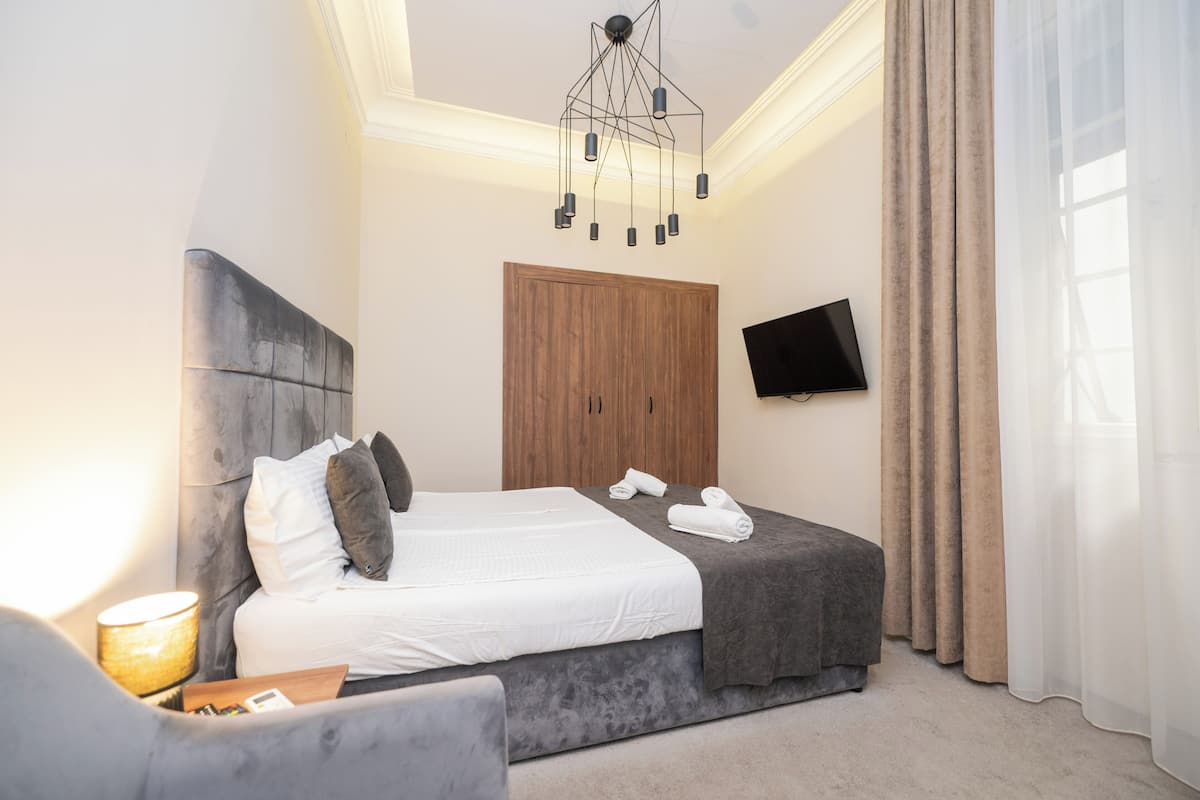 Ein modernes Hotelzimmer mit einem großen Bett, einem Holzschrank, einem Flachbildfernseher und einem Nachttisch mit Lampe.