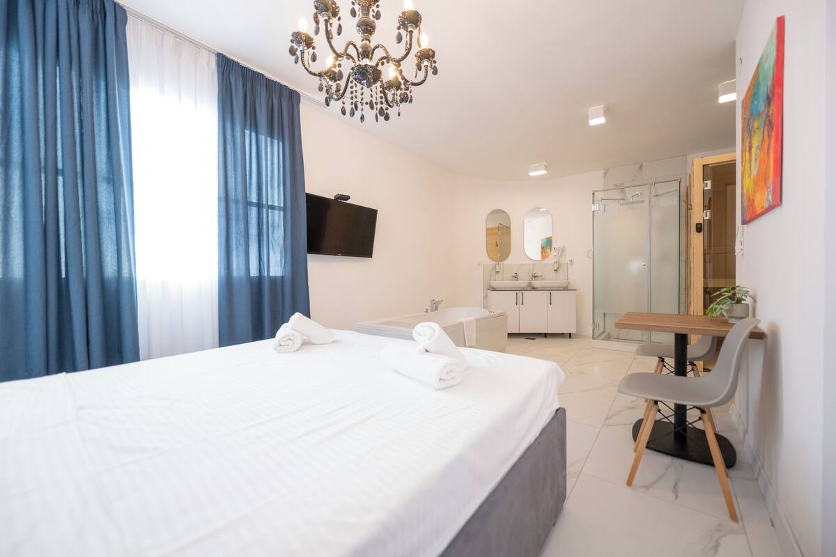 Ein modernes Hotelzimmer mit einem großen Bett, einem Schreibtisch, einem Badezimmer mit Dusche und einem an der Wand montierten Fernseher.