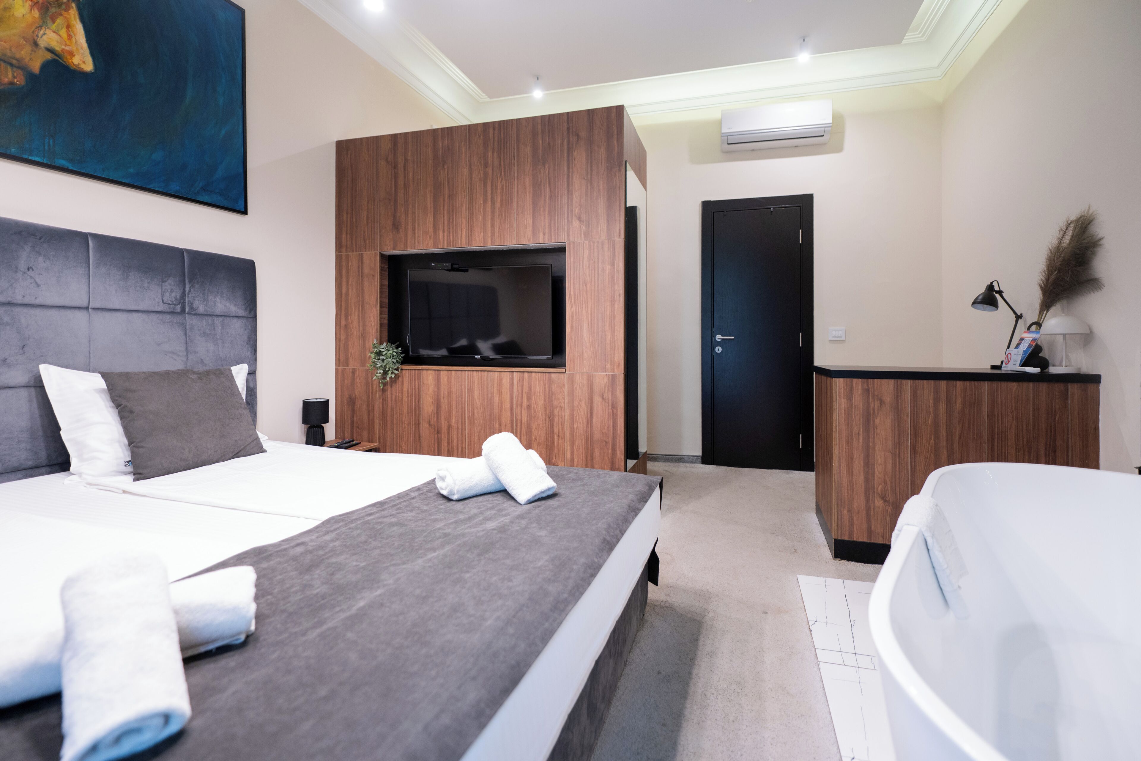 A modern hotel room with a large bed, a flat-screen TV, a wooden accent wall, a desk, and a bathroom.