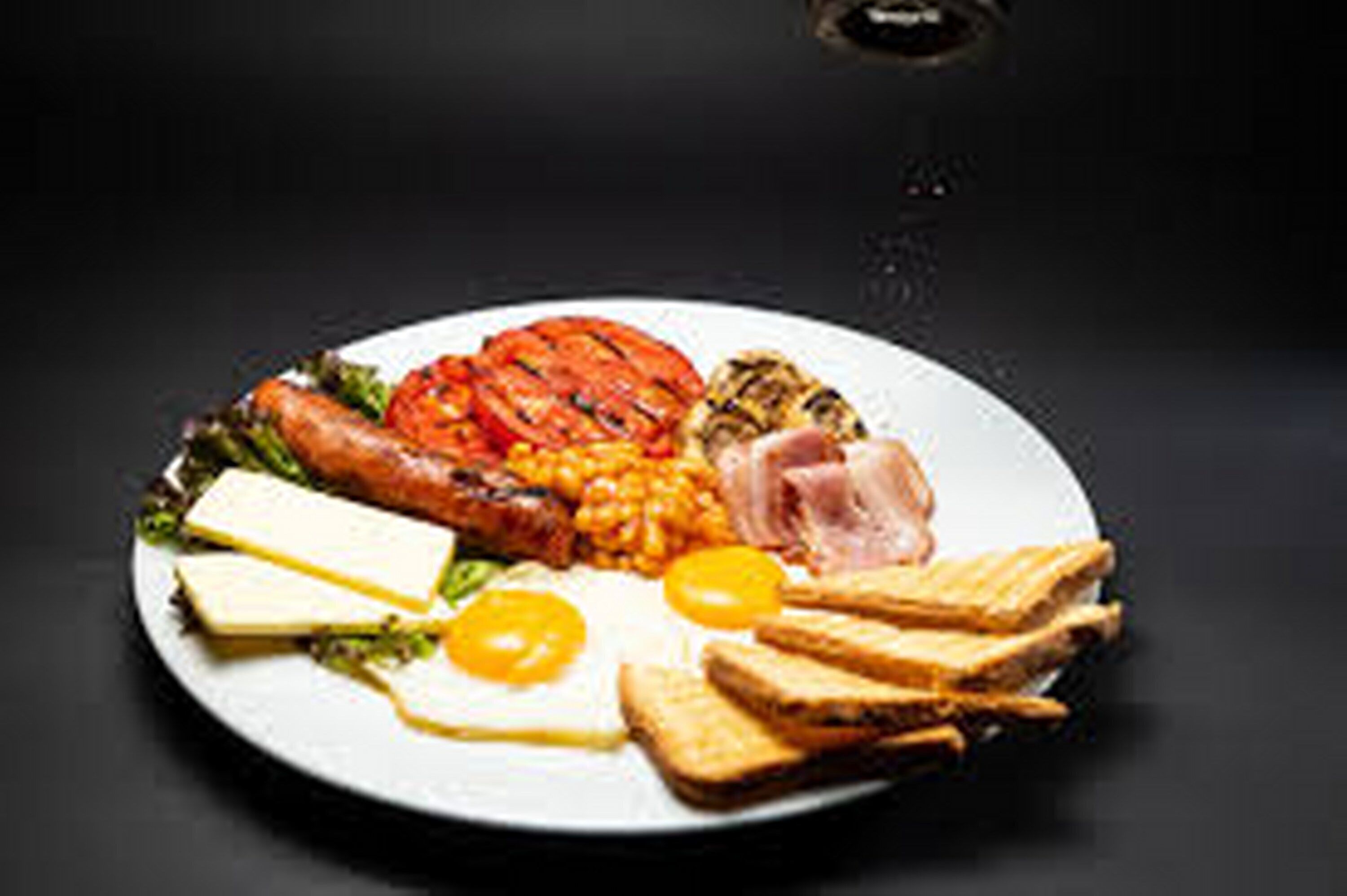 Une assiette de nourriture pour le petit-déjeuner comprenant des œufs, des toasts, des saucisses et des tomates.