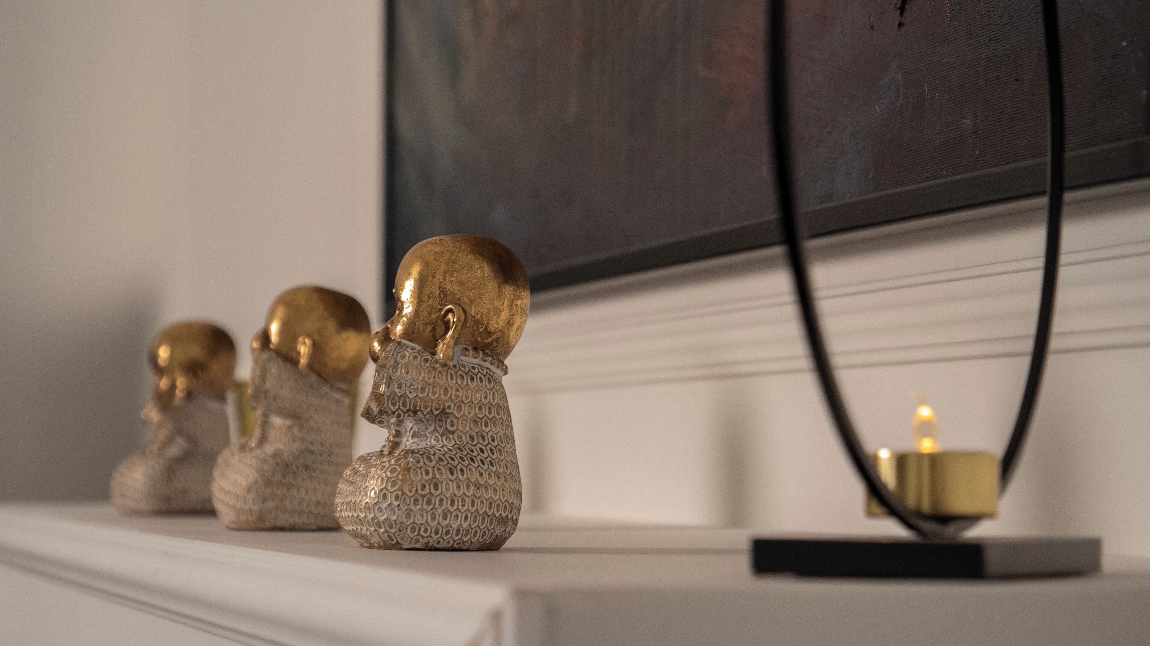 Three golden busts on a white shelf, a wall-mounted TV, and a candle on a black base.
