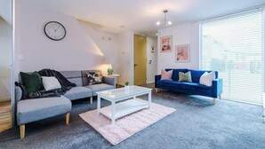 A living room with two sofas, a coffee table, a clock, and a window with blinds.