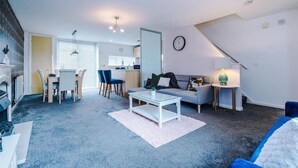 A modern apartment with a living room, dining area, and kitchen. There is a staircase leading to an upper level.
