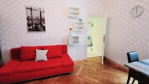 A room with a red sofa, a wooden floor, a white wall with shelves, a door, and a clock. - Wipplinger Home Apartment Vienna (Vienna)