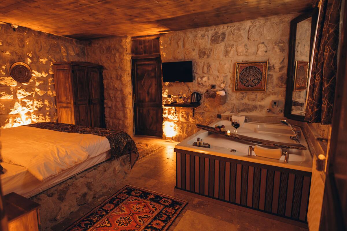 Ein rustikaler Raum mit Steinwand, Holzbett und einer großen Badewanne.