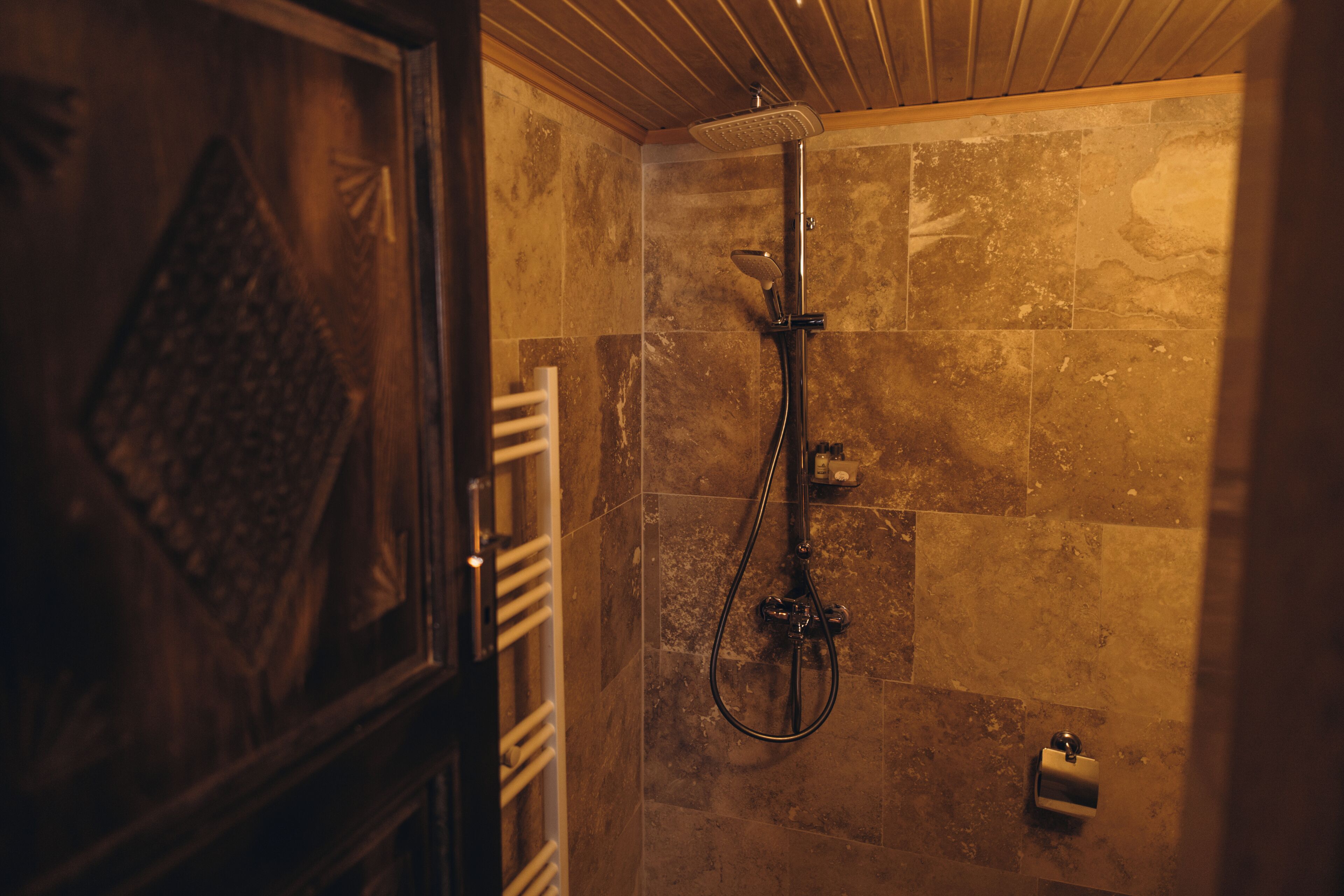 Eine Dusche mit Handbrause, Armatur an der Wand, Handtuchhalter und Seifenspender.