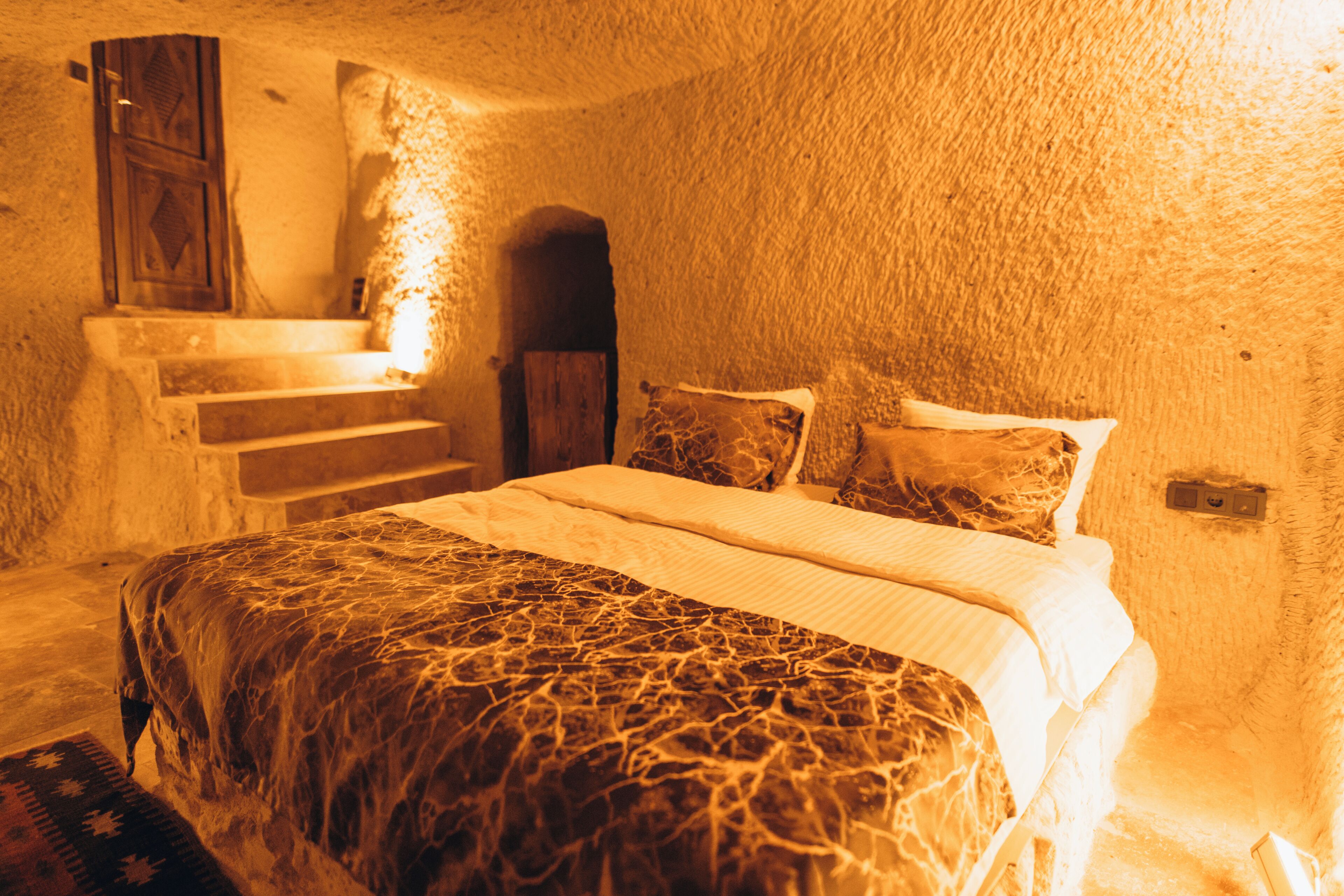 A bedroom with a bed, pillows, a blanket, a wooden door, and a staircase leading to a higher level.
