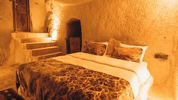 A bedroom with a bed, pillows, a blanket, a wooden door, and a staircase leading to a higher level.