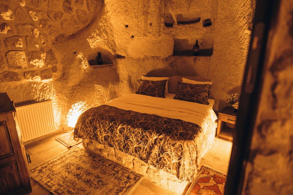 Ein Schlafzimmer mit Steinwänden, einem Bett, Kissen und einem Nachttisch.