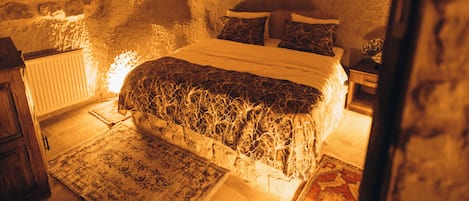 Un dormitorio con paredes de piedra, una cama, almohadas y una mesita de noche.