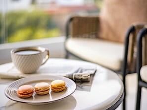 A table with a cup of coffee and three macarons on a plate, a book, and a chair in the background. - Sanders Olive Shared Pool Apartments (Paphos)