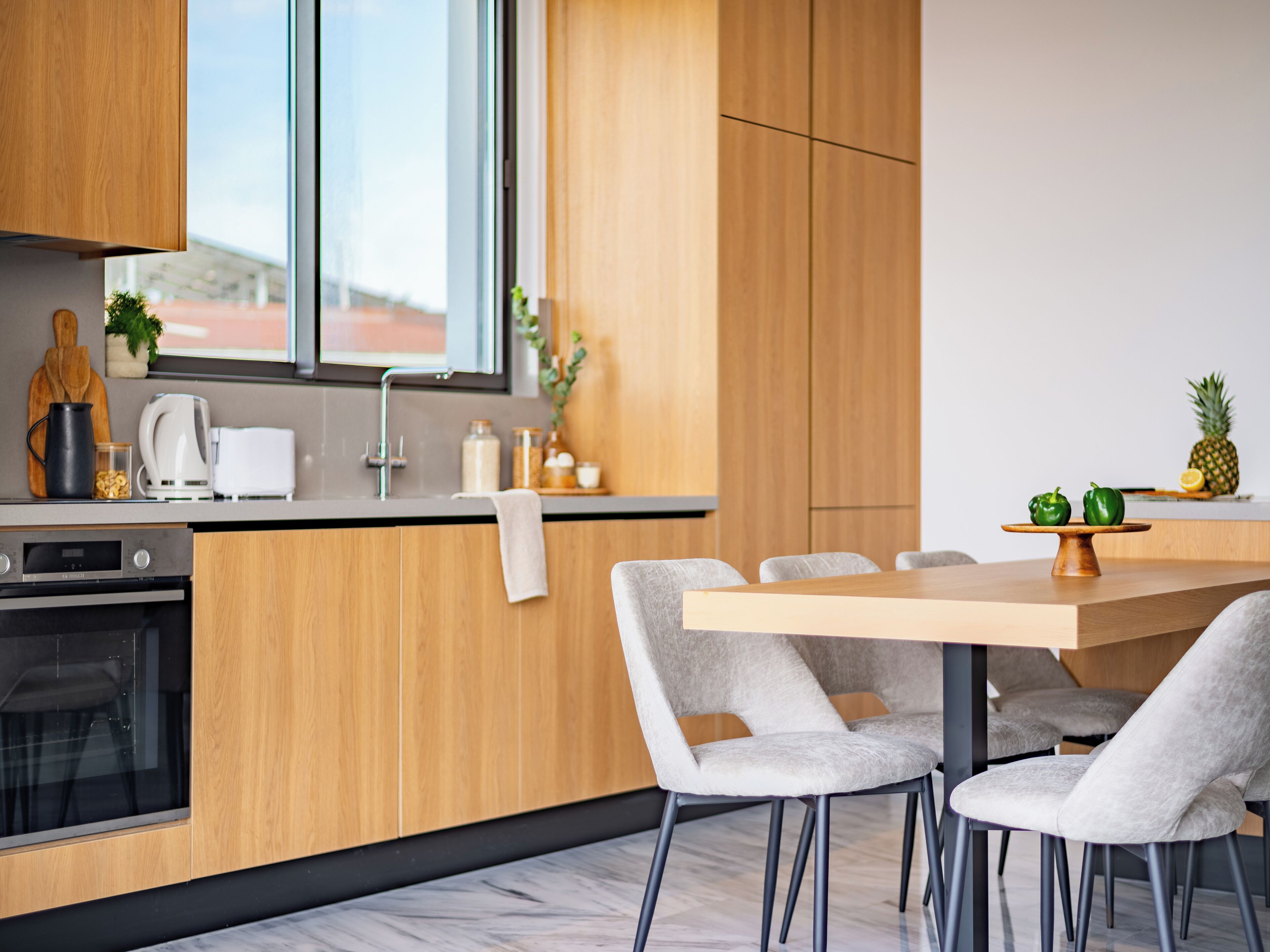 Eine moderne Küche mit Holzschränken, einem eingebauten Ofen und einem Essbereich mit grauen Stühlen und einem Holztisch.
