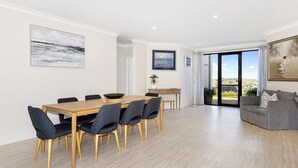 Amplia sala de estar con una mesa y sillas de madera, un sofá gris y un ventanal con vistas al exterior.