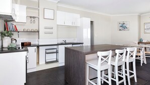 Una cocina moderna con armarios blancos, una isla central y una zona de comedor con sillas blancas.