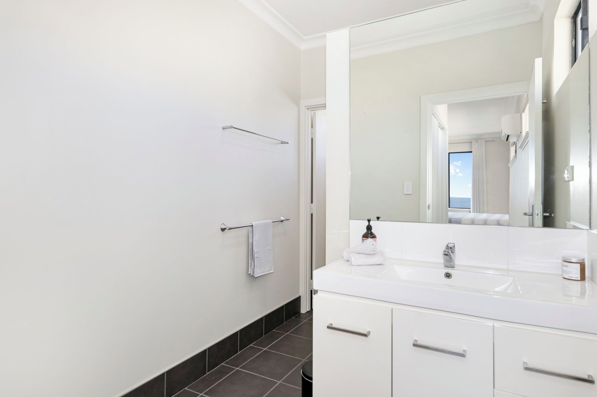 Een moderne badkamer met een witte wastafel, een grote spiegel en een handdoekhouder.