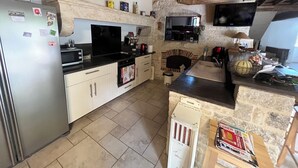 A kitchen with a stone wall, wooden beams, a refrigerator, a stove, and a sink.