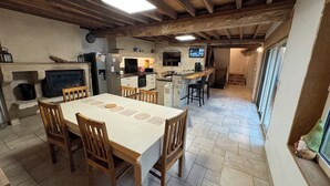 A rustic kitchen with a dining area, stone walls, wooden beams, and a stone fireplace.