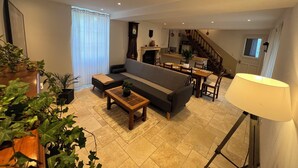 A modern living room with a sofa, coffee table, and dining table. There is a staircase leading to an upper level.