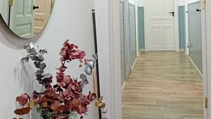 Un pasillo con una puerta blanca al final, un espejo en la pared y un florero con flores sobre una mesa.