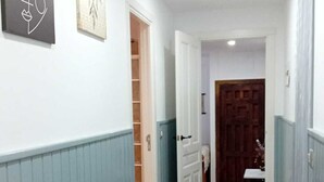 Un pasillo con piso de madera, paredes blancas y una puerta que da a una habitación.