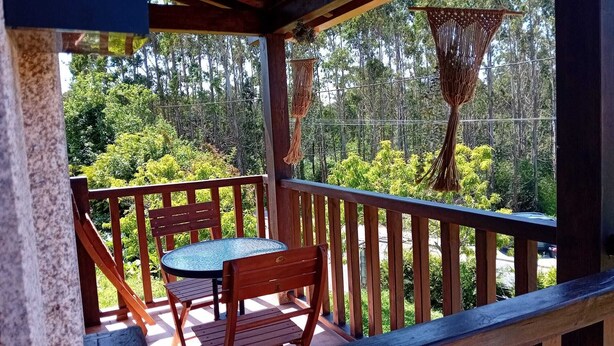 Una terraza de madera con una mesa y sillas, rodeada de abundante vegetación y árboles.