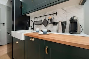 A modern kitchen with dark green cabinets, a white countertop, and a marble backsplash.