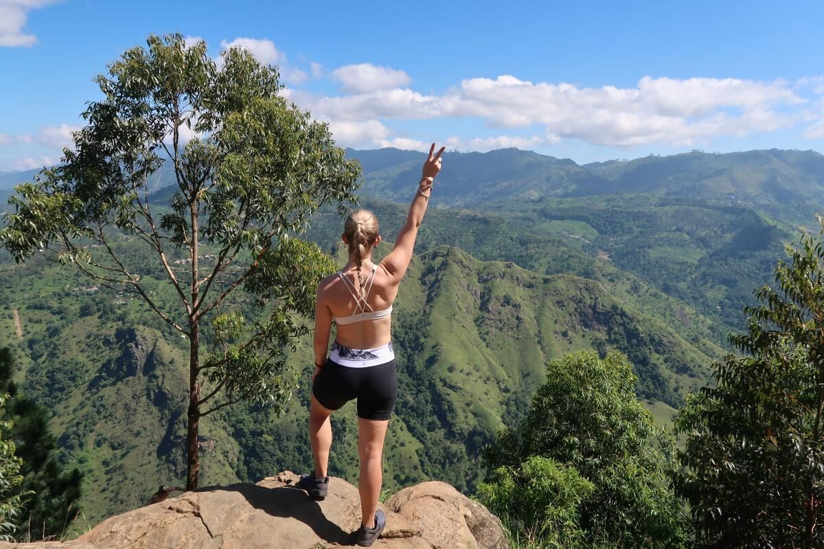 A person standing on a rock with a scenic view of green hills and a clear sky.