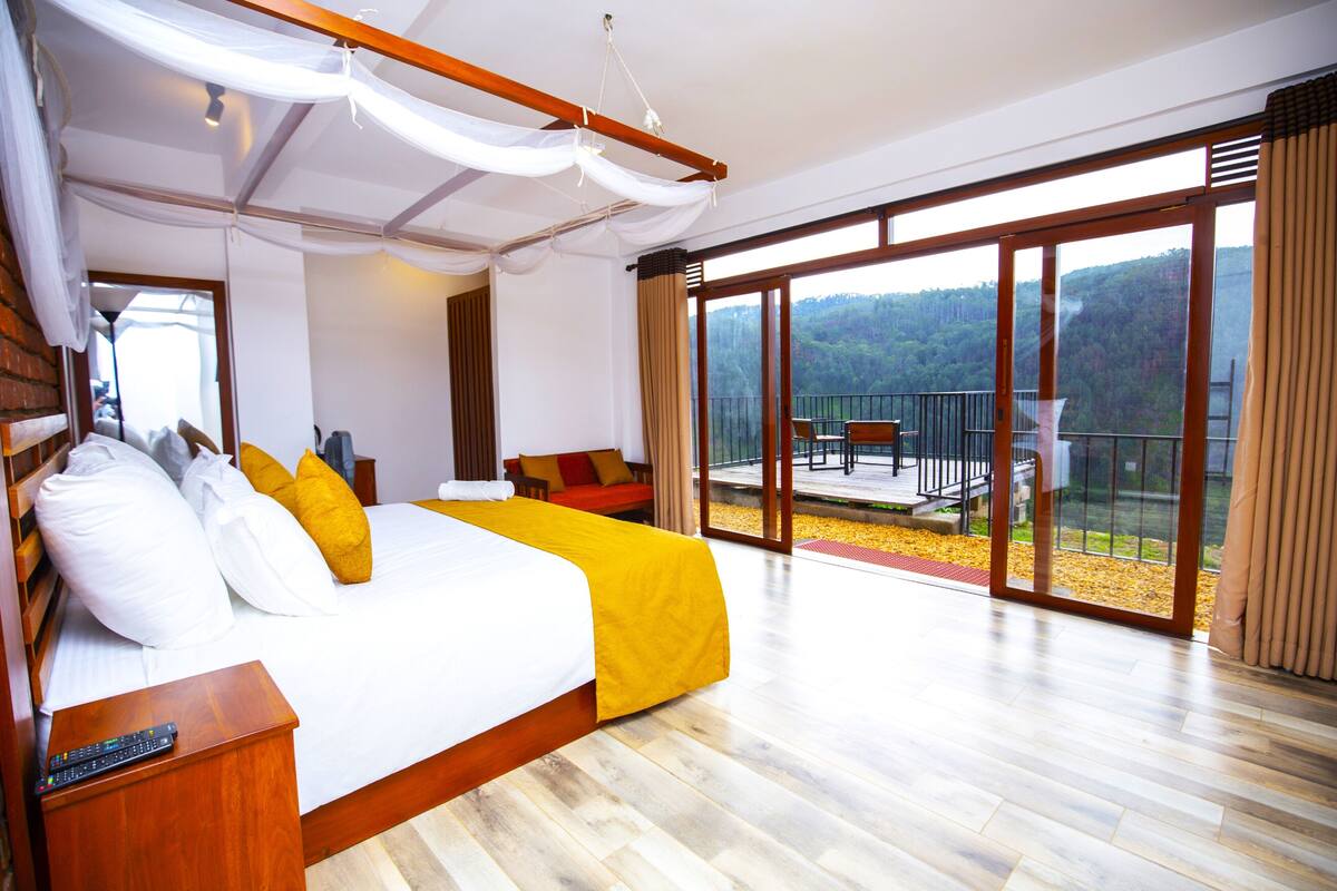 Ein geräumiges Schlafzimmer mit einem großen Bett, einem Balkon mit Blick auf den Wald und einer separaten Sitzecke.
